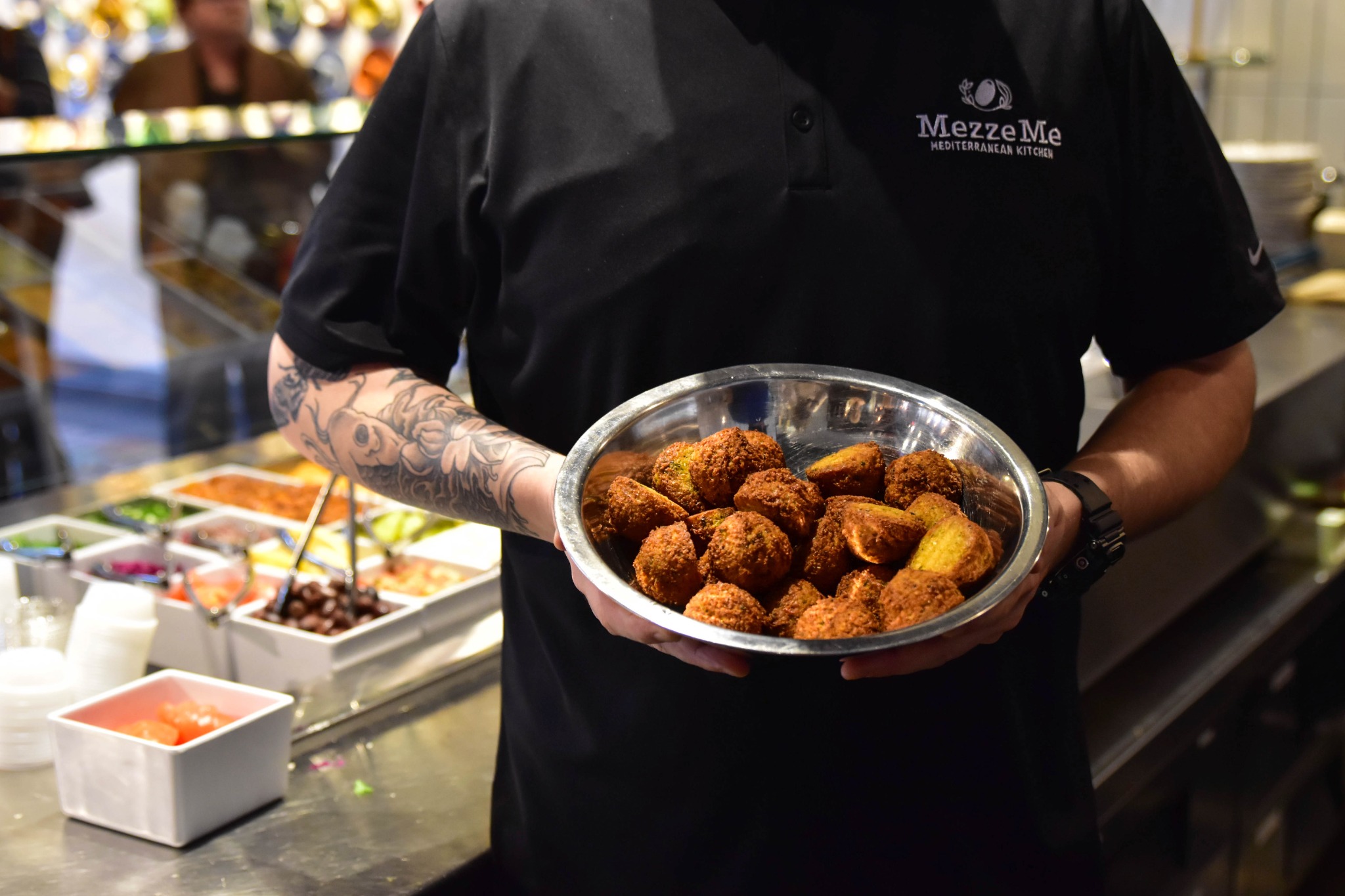 A MezzeMe team member holding a bowl of falafel